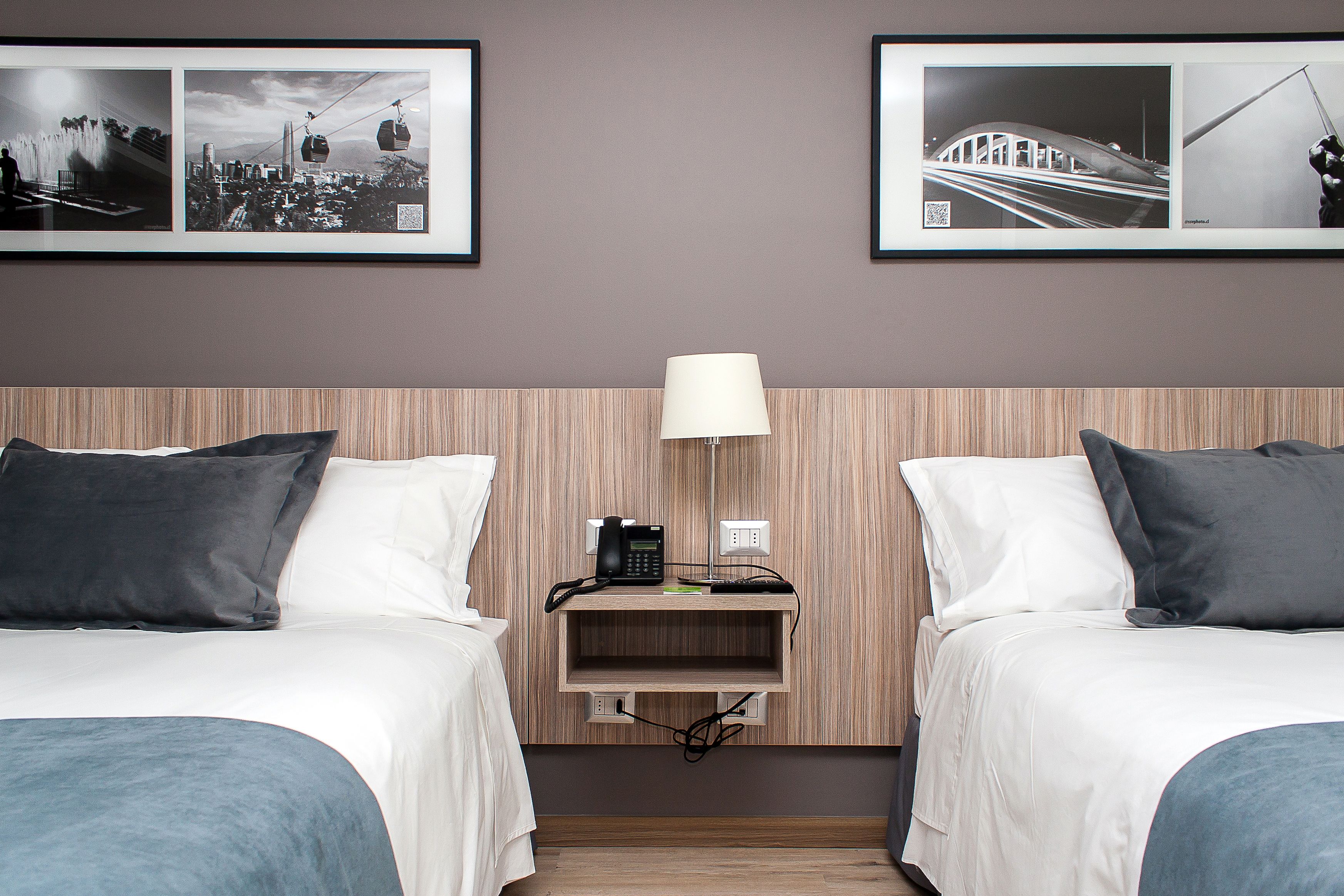 A hotel room with two beds, a nightstand with a lamp, and framed pictures on the wall.