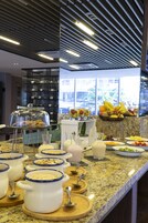 A buffet setup with various food items and beverages, a wine rack in the background, and a modern ceiling design.