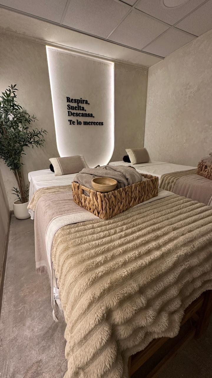 A bedroom with two beds, a wall-mounted light, a potted plant, and a wall with a motivational quote.