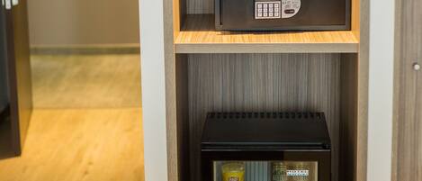 A hotel room with a minibar, a small refrigerator, a vase with flowers, and towels on the table.