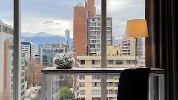 A hotel room with a bed, a desk, and a lamp. The room has large windows with a view of a cityscape and mountains.