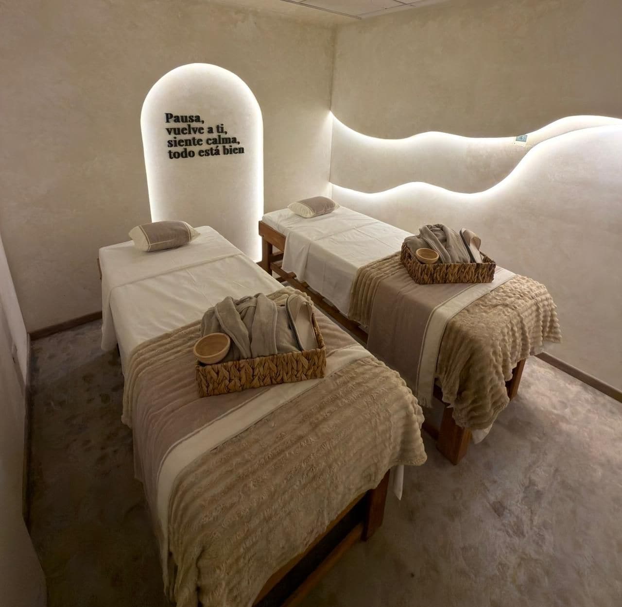 Un cuarto de spa con dos camas, una silla de masaje fija a la pared y una cesta de toallas.