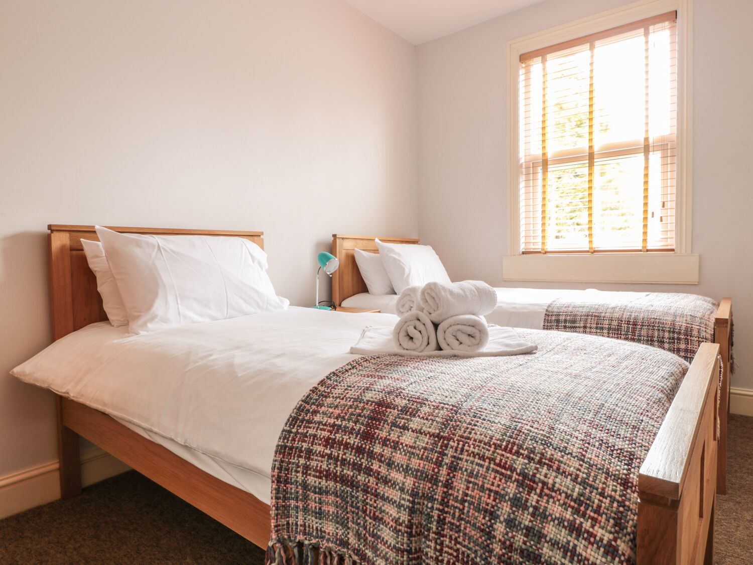 Quarto de hotel com duas camas, uma janela grande e uma cama bem arrumada com toalhas dobradas.