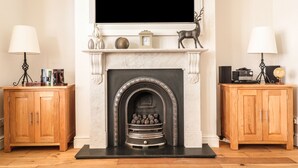 A living room with a fireplace, two wooden cabinets, and a television mounted above the fireplace. - 33 Crescent Gardens (Bath)