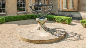 A sculpture of a metallic sphere on a pedestal in a courtyard with a building in the background. - 33 Crescent Gardens (Bath)