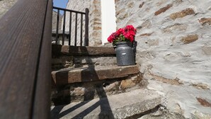 A stone building with a wooden staircase and a metal bucket with red flowers. - Mill Dam Farm Cottage (Lancaster)