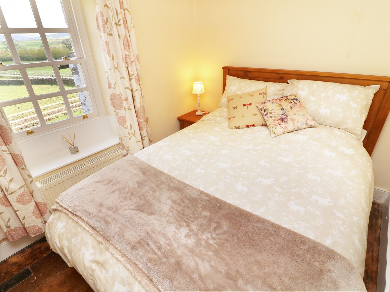 A bedroom with a bed, a nightstand, a lamp, a window with curtains, and a radiator.