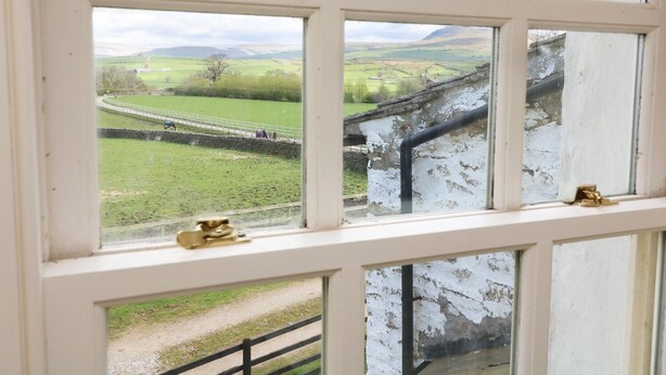A view through a window with a rural landscape, including fields, a stone wall, and a distant hill. - Mill Dam Farm Cottage (Lancaster)