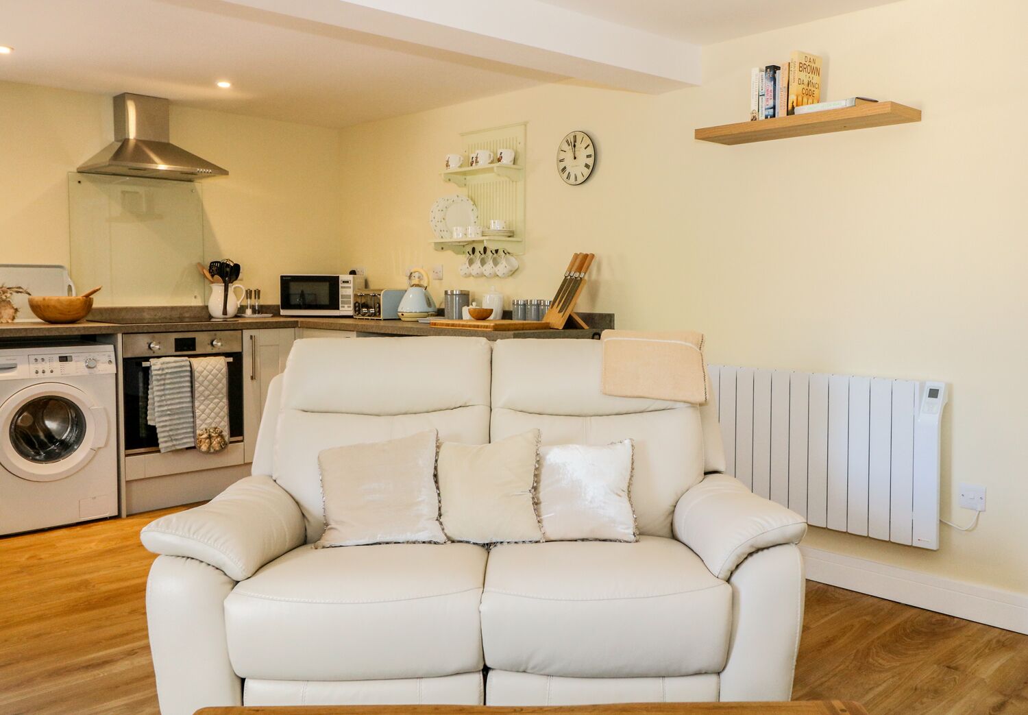En moderne stue med en hvid lædersofa, en vaskemaskine, en mikrobølgeovn og en radiator.