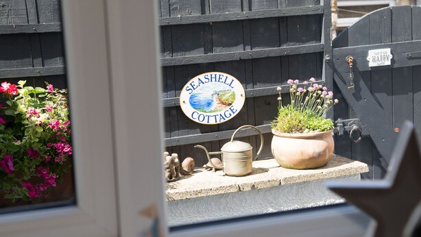 A sign for Seashell Cottage, a wooden fence, a potted plant, and a small decorative item.