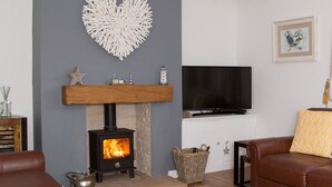 A living room with a stone fireplace, a television, a brown leather sofa, and a heart-shaped wall decoration.