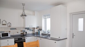 A modern kitchen with white cabinets, a microwave, a kettle, and a wooden dining table.