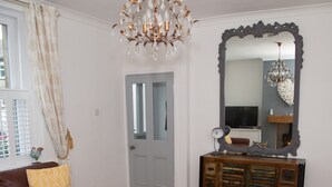 A living room with a brown leather sofa, a wooden console table, a large ornate mirror, and a chandelier.