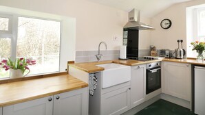 A modern kitchen with a wooden countertop, stainless steel appliances, a window with a view, and a clock on the wall. - Annfield (Aberlour)