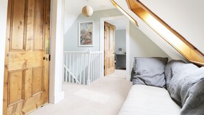 A bedroom with a sloped ceiling, a bed with grey bedding, a wooden door, and a white railing. - Annfield (Aberlour)