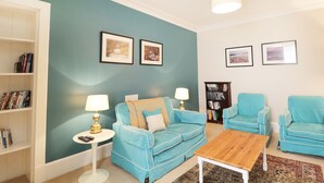 A living room with teal walls, a blue sofa, a wooden coffee table, and a bookshelf. - Annfield (Aberlour)