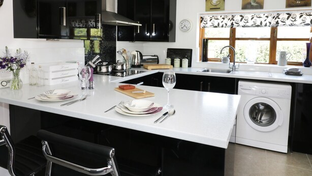 A modern kitchen with black cabinets, a white countertop, a built-in washing machine, and a window with a view of greenery.