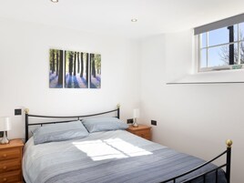 A bedroom with a bed, two bedside tables, a window, and a wall-mounted picture of a forest.