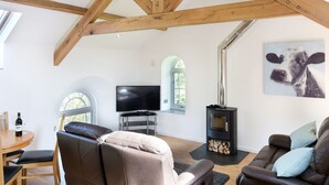 A spacious living area with high ceilings, exposed wooden beams, a fireplace, a television, and comfortable seating. - Moor View Chapel (Camelford)