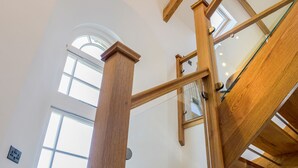 A wooden staircase with glass railings inside a building with large windows. - Moor View Chapel (Camelford)