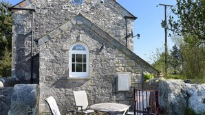 A stone building with a small window, outdoor seating, and a metal gate. - Moor View Chapel (Camelford)