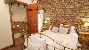A bedroom with a stone wall, a wooden door, a bed with white bedding, and two bedside tables with lamps. - Clove Cottage (Appleby-in-Westmorland)