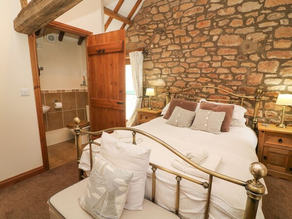 A bedroom with a stone wall, a wooden door, a bed with white bedding, and two bedside tables with lamps.