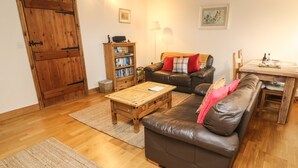 A cozy living room with a brown leather sofa, a wooden coffee table, and a bookshelf. - Clove Cottage (Appleby-in-Westmorland)