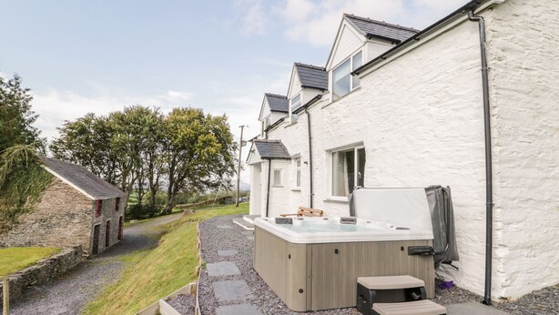 A modern outdoor hot tub area adjacent to a white building with a stone pathway leading to it. - Bryndan (Machynlleth)