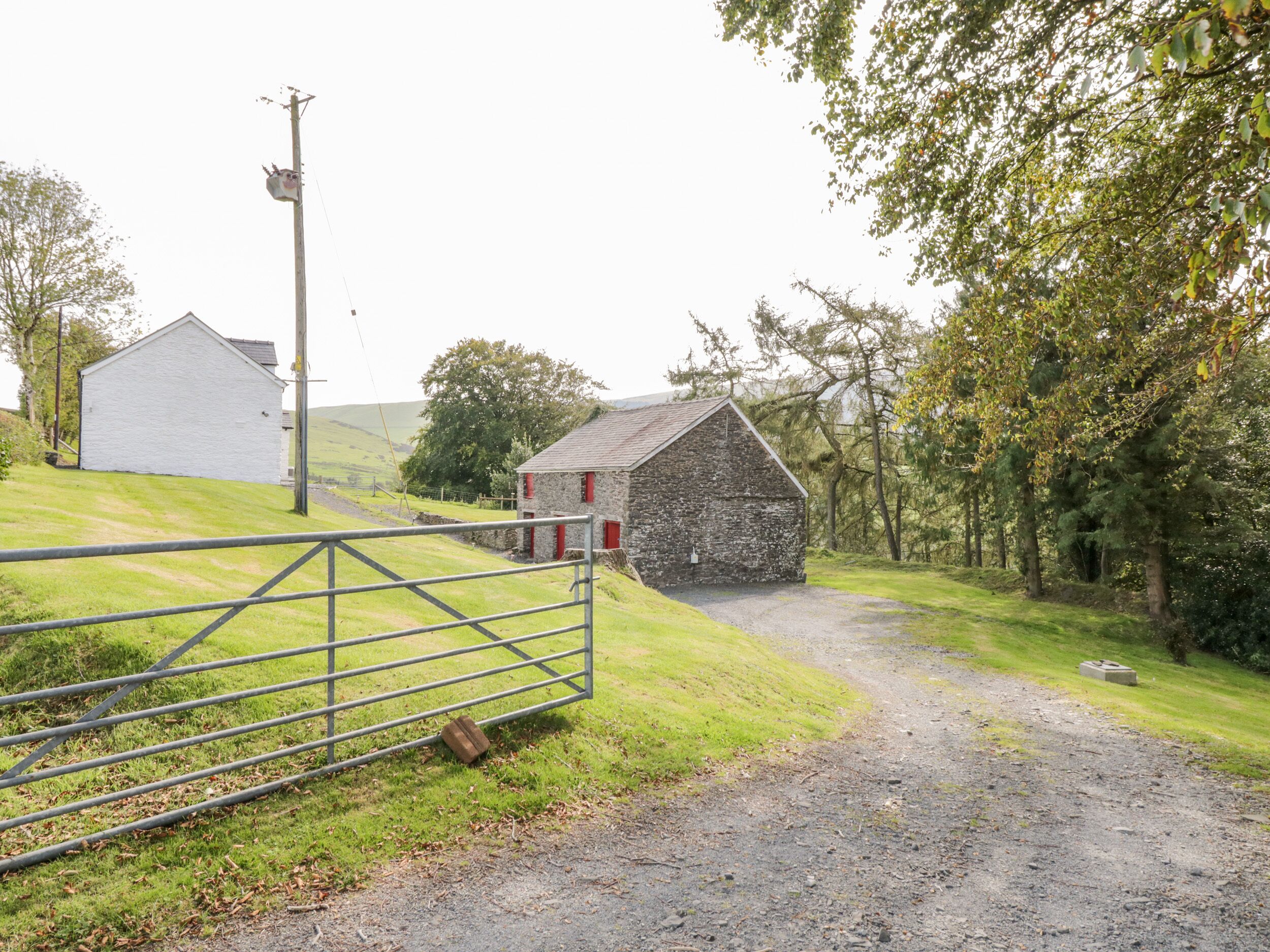 A rural landscape with a stone barn, a white building, and a metal gate.