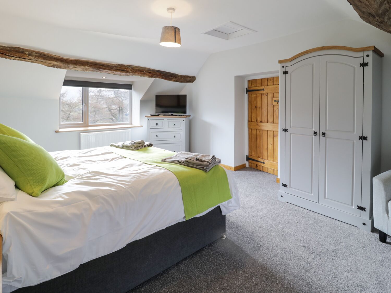 A bedroom with a bed, a TV, a wardrobe, and a window.