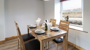 A dining area with a wooden table set for four, equipped with plates, cutlery, and a bottle of wine. The room has a large window with a view of the outdoors. - Bryndan (Machynlleth)
