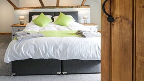A bedroom with a bed, two bedside tables, a nightstand, a wooden door, and exposed wooden beams on the ceiling. - Bryndan (Machynlleth)