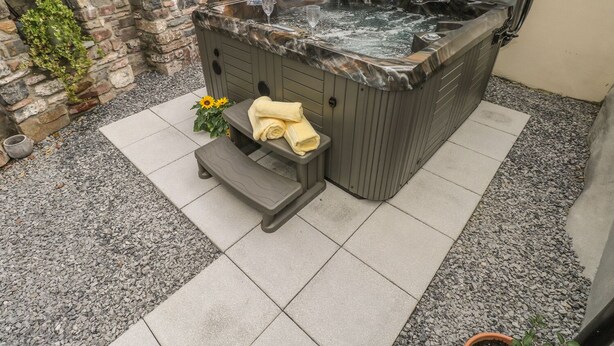 Un bain à remous avec un mur de pierres en arrière-plan, un petit banc avec des serviettes et une plante en pot.