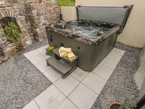Un bain à remous avec un mur de pierres en arrière-plan, un petit banc avec des serviettes et une plante en pot.