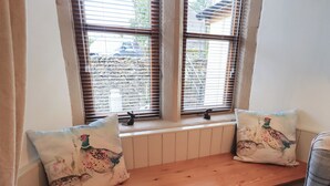 Un siège de fenêtre agrémenté de deux coussins, un radiateur en dessous, et une vue sur l’extérieur.