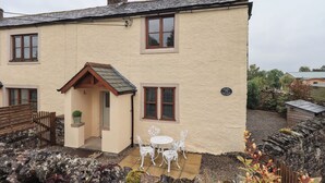 Une maison à deux étages avec un petit porche et un patio aménagé avec des chaises en métal blanc.