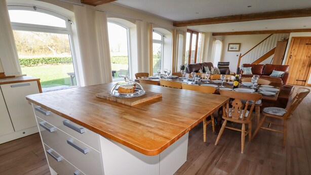 A spacious kitchen with a wooden countertop, white cabinetry, and a dining area with wooden chairs and a table set for four. - The Oaks (Ellesmere)