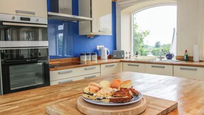 A modern kitchen with a wooden countertop, a built-in oven, and a large window providing natural light. - The Oaks (Ellesmere)
