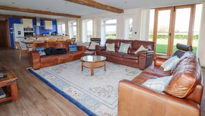 A spacious living room with a brown leather sofa set, a coffee table, and a dining area with wooden chairs. - The Oaks (Ellesmere)