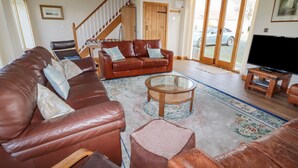 A living room with a brown leather sofa, a wooden coffee table, and a television on a wooden stand. - The Oaks (Ellesmere)
