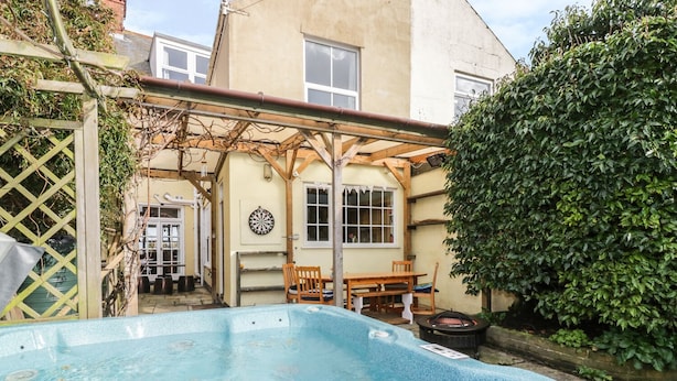 Un jardin avec une piscine, une pergola en bois, un jeu de fléchettes et une table à manger.