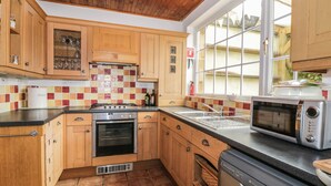Une cuisine avec des meubles en bois, un pare-feu en carrelage, une cuisinière, un four, un lave-vaisselle et une fenêtre donnant sur l’extérieur.