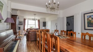 Une salle à manger spacieuse avec une table et des chaises en bois, un piano et un lustre.