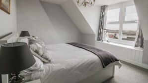 Une chambre à coucher avec un lit, une lampe, un lustre, une fenêtre avec des rideaux et un télescope posé sur le rebord de la fenêtre.