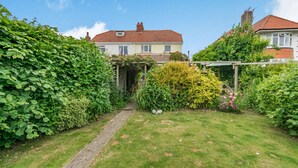 A residential garden with a pathway leading to a house with a red roof and white walls. - The Perks (Scarborough)