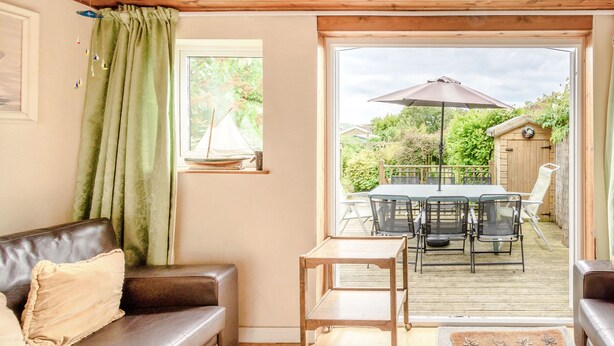 A cozy living room with a brown leather sofa, a small wooden table, and a view of an outdoor patio with a table and chairs. - The Perks (Scarborough)