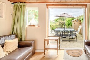 A cozy living room with a brown leather sofa, a small wooden table, and a view of an outdoor patio with a table and chairs.