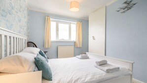 A bedroom with a white bed, a window with curtains, a radiator, and a wall-mounted light fixture. - The Perks (Scarborough)