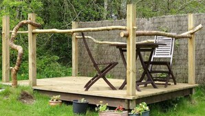 Un muelle de madera con un columpio y una silla, rodeado de follaje.